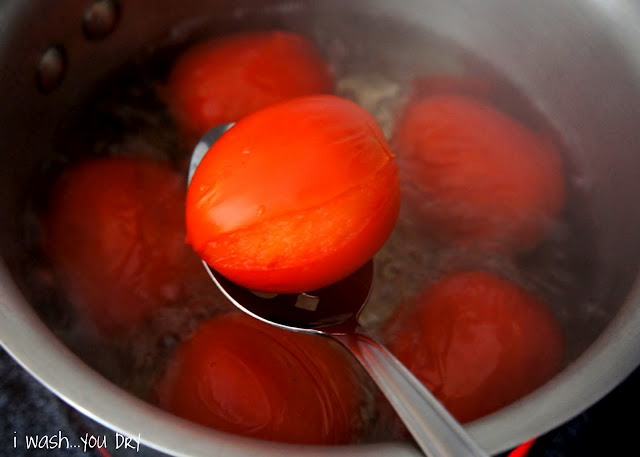 A spoon holding a Roma tomato above a pot of boiling water with more tomatoes in it