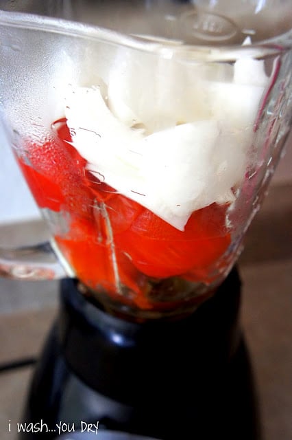 A blender with tomatoes and onions in it