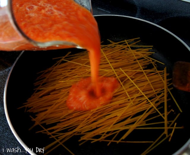 A red sauce being poured over noodles in a skillet