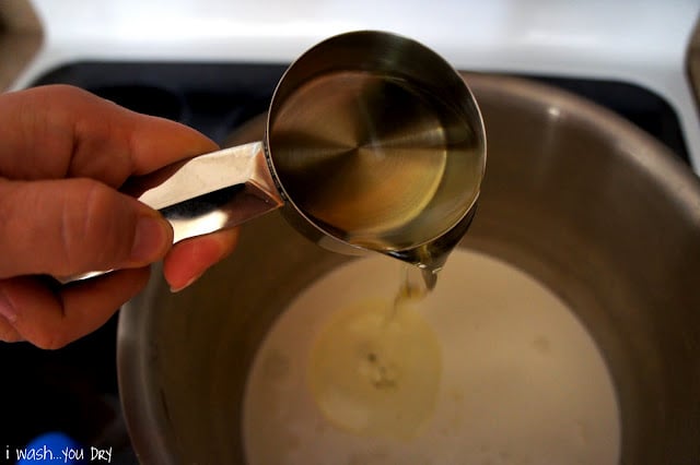 A hand pouring a measuring cup of oil into a pot of ingredients