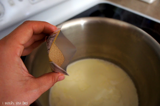 A hand adding a package of dry yeast to liquid in a pot