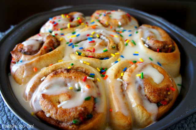 A close up of cinnamon rolls in a round pan topped with icing and sprinkles