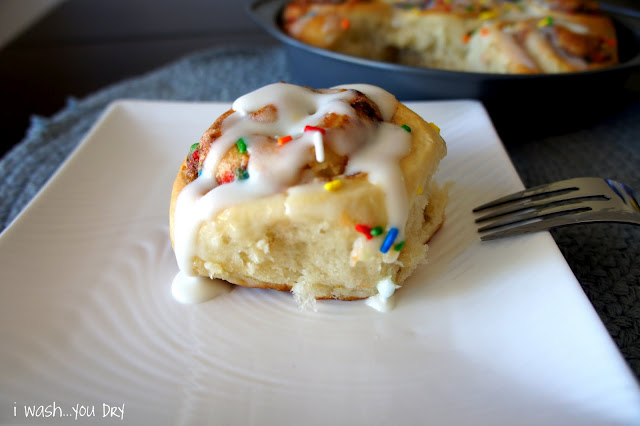 A cinnamon roll with icing and sprinkles displayed on a plate