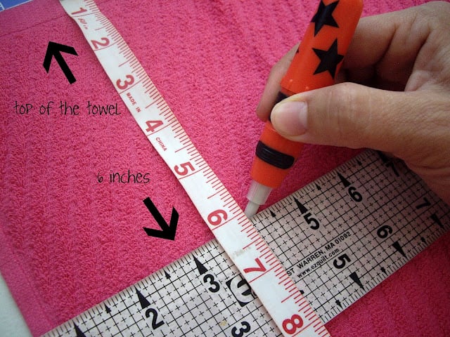 A hand measuring and marking a length on a dish towel. 
