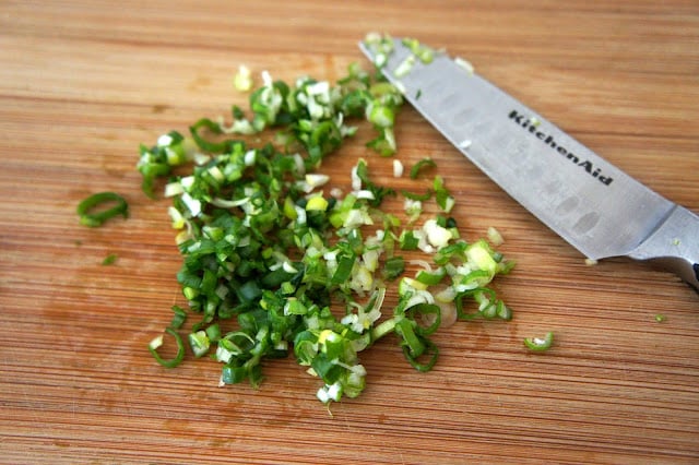Chopped green onions on a cutting board in a pile next to a knife