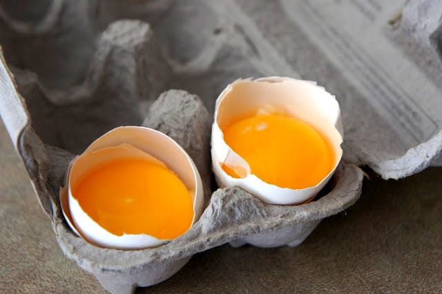 Two egg yolks resting in half an egg shell in the egg carton, separated from the egg whites