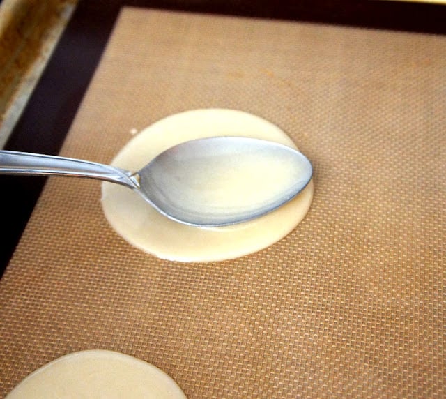 A spoon spreading the batter into a circle on the baking pan