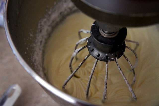 A close up of a beater in a mixing bowl mixing the frosting
