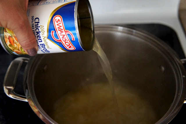 A hand pouring a can of Chicken Broth into a pot