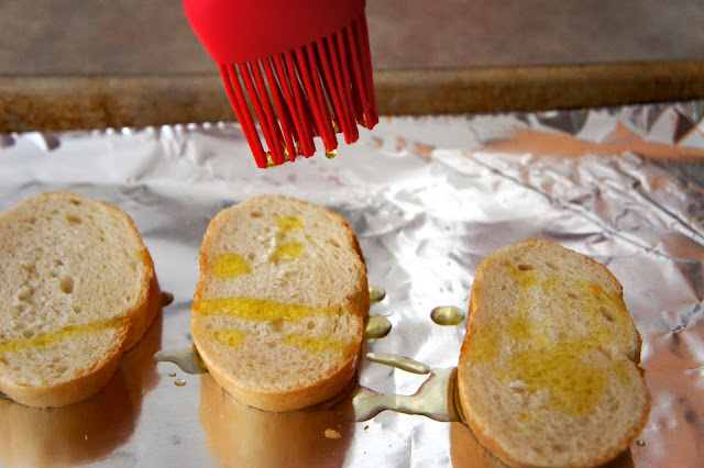 Oil being brushed onto slices of French bread laying pan tinfoil lined pan