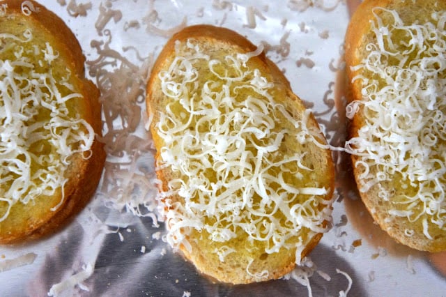 A close up of a slice of French bread topped with oil and shredded cheese