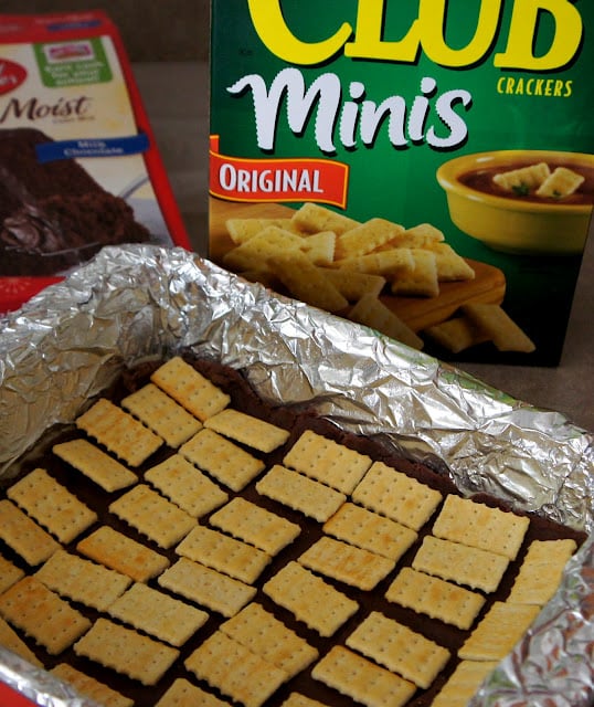 A tinfoil lined baking dish with brownie dough topped with club crackers