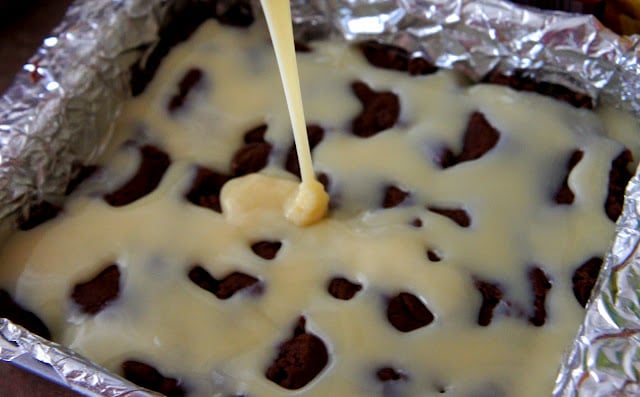 A liquid being poured on top of raw brownie dough pressed into a tinfoil lined baking dish