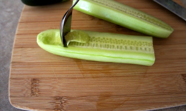 A spoon removing the seeds of half of a peeled cucumber