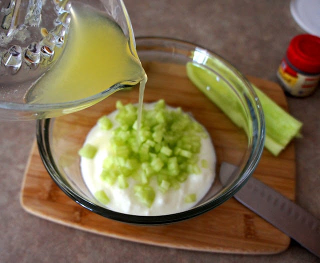 Lemon juice being poured over a bowl of white sauce and diced cucumber