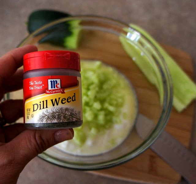 A bottle of Dill Weed in front of a bowl of white sauce and diced cucumbers