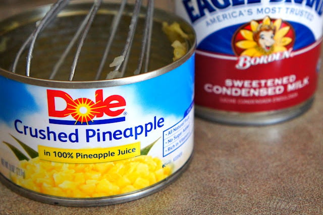 A close up of an open can of crushed pineapples next to a can of sweetened condensed milk