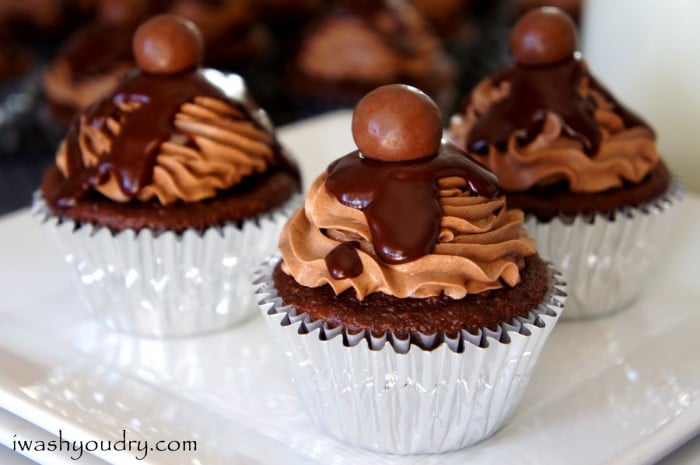 A close up of chocolate cupcakes on a table topped with a chocolate frosting, drizzled chocolate and a chocolate ball