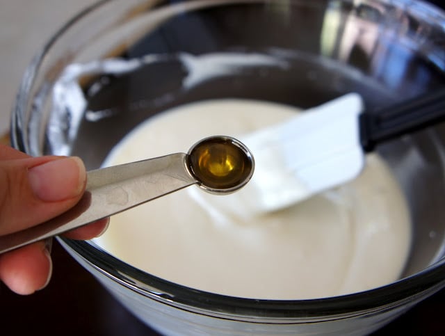 A measuring spoon of cinnamon oil over a bowl of melted white chocolate