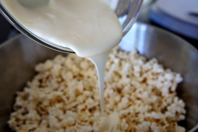 A close up of melted white chocolate being poured over popcorn