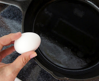 A hand holding an egg over a skillet