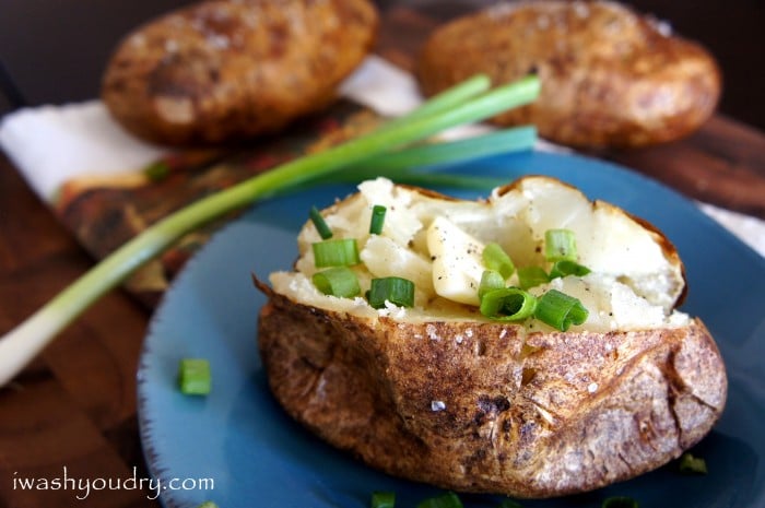 A close up of a baked potato on a plate, sliced open and topped with chives