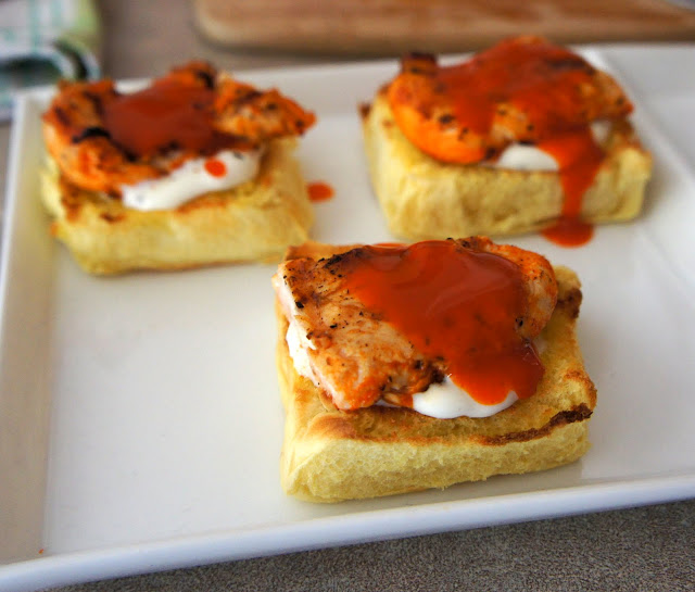 A close up of a plate with 3 halves of a roll topped with white sauce, a small portion of chicken and a red sauce