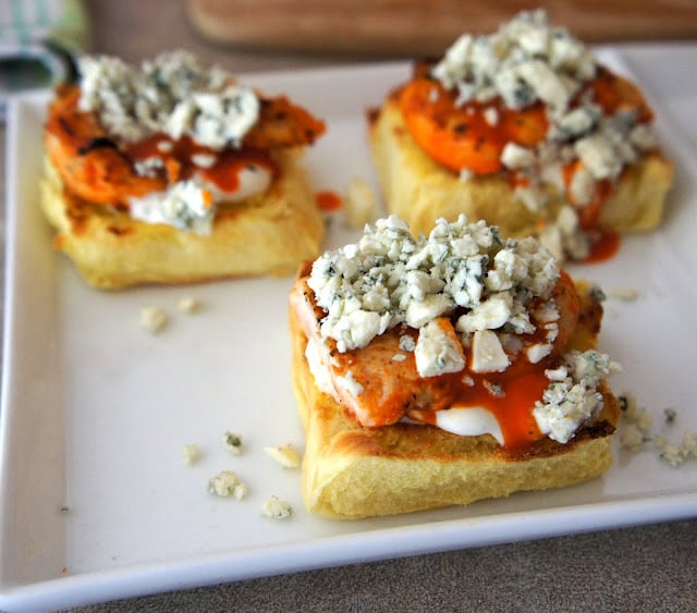 A plate with three slider halves, each topped with white sauce, chicken, red sauce and blue cheese