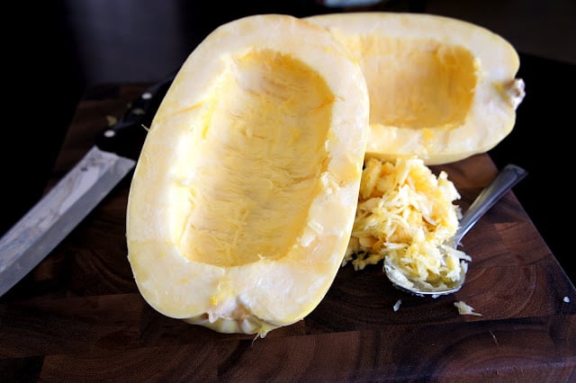 A spaghetti squash cut in half with no seeds in the centers and a pile of seeds next to them on the cutting board