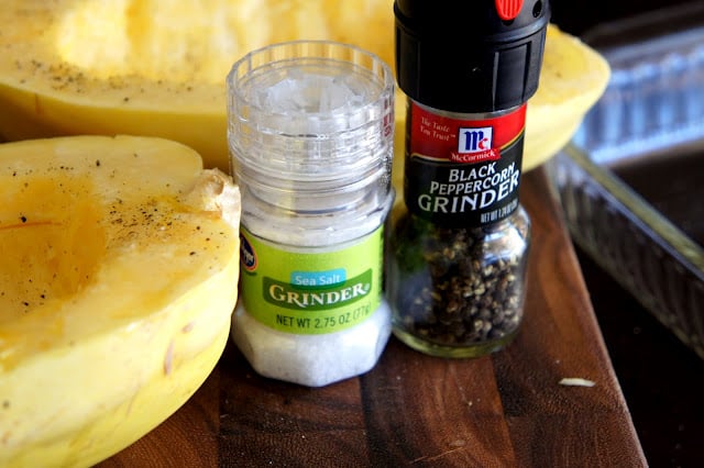 A close up of salt and pepper next to spaghetti squash prepared for baking