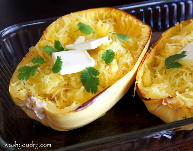 Baked spaghetti squash in a pan with a couple squares of melting butter and herbs on it.