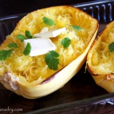 Baked spaghetti squash in a pan with a couple squares of melting butter and herbs on it.