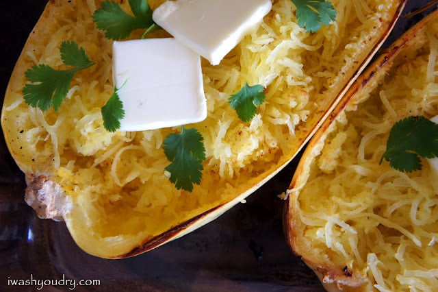 A close up of baked spaghetti squash with a couple squares of melting butter and herbs on it.