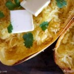 A close up of baked spaghetti squash with a couple squares of melting butter and herbs on it.