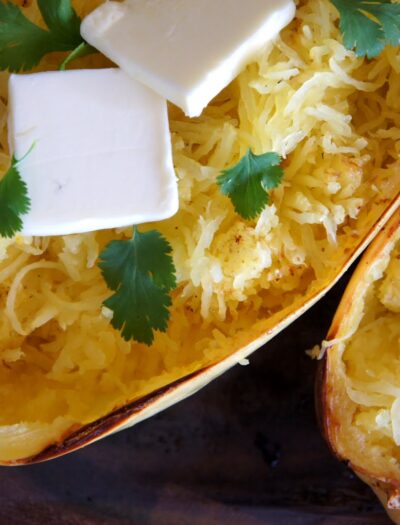 A close up of baked spaghetti squash with a couple squares of melting butter and herbs on it.