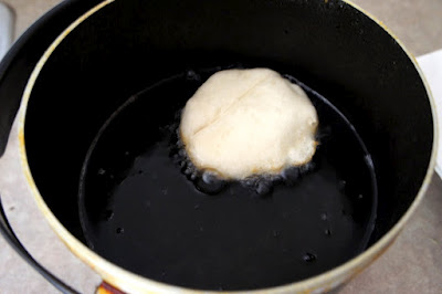 A pan filled with oil and a raw biscuit frying in it