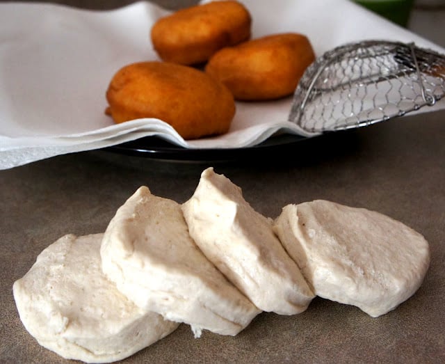 A raw biscuit dough slices lined up in front of a plate with fried biscuits 