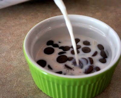 Warm milk being poured into a small bowl of chocolate chips