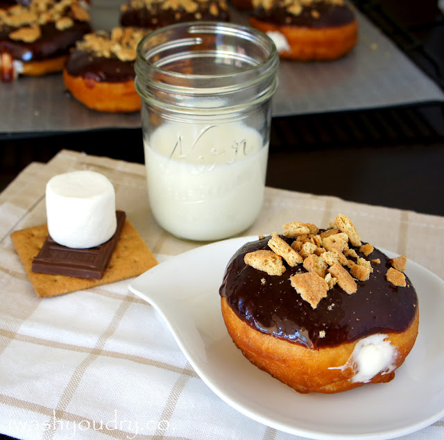 A Marshmallow Cream filled S\'mores Doughnut displayed on a plate next to a glass of milk and an uncooked S\'more