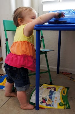 A little girl standing next to a kid table with her hand reaching onto a plate