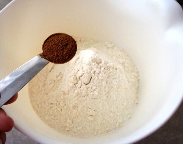 A measuring spoon with cinnamon above a bowl of flour mixture