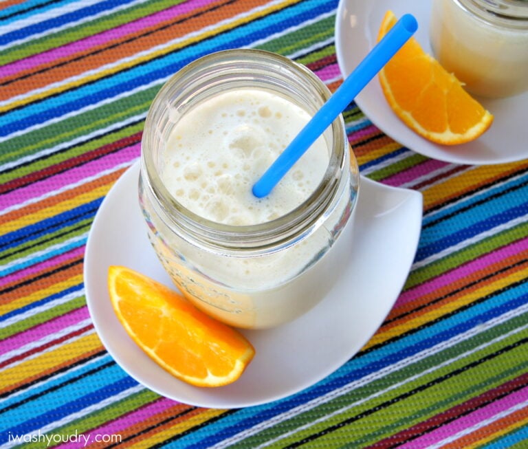 A close up look into a mason jar filled with Pineapple Orange Julius on a plate next to a slice of orange
