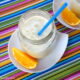 A close up look into a mason jar filled with Pineapple Orange Julius on a plate next to a slice of orange