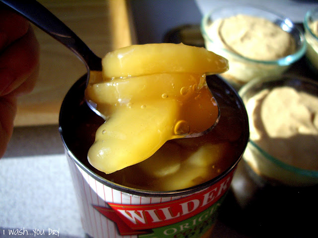 A spoon pulling apples from a can of apple pie filling. 