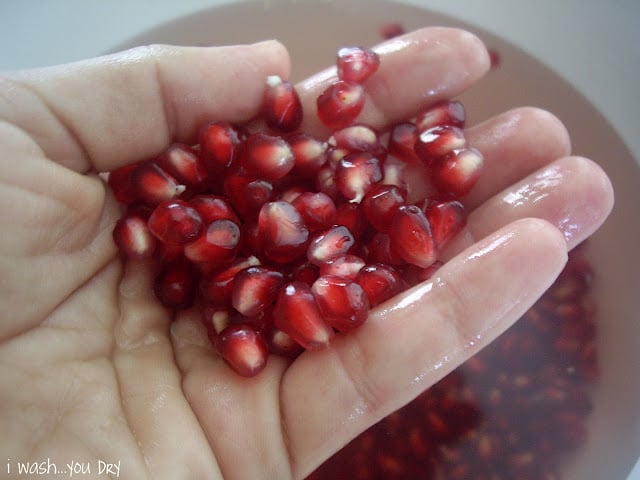 A hand holding pomegranate seeds above a bowl of more seeds.