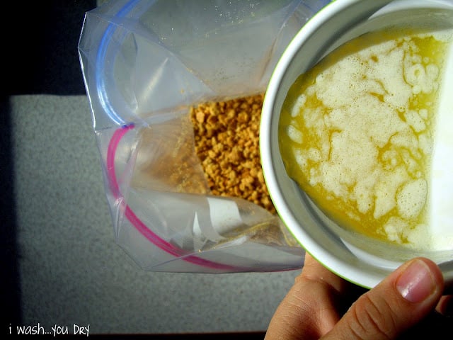 A bowl of melted butter being added to a ziplock bag of crushed graham cracker. 