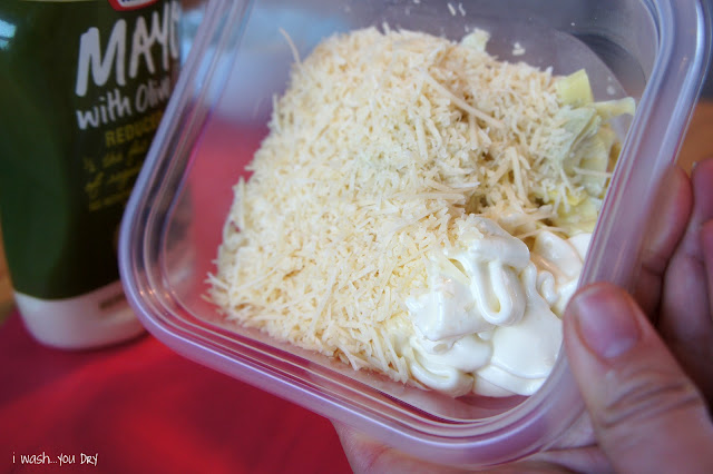A plastic container with mayo, cheese and chopped artichokes in it. 