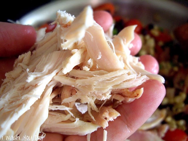 A hand adding shredded chicken to a pan. 