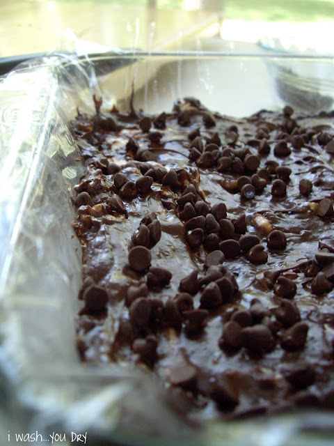 A close up of fudge spread into a plastic lined glass dish sprinkled with chocolate chips. 