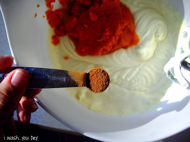 A measuring spoon of cinnamon above a bowl of batter. 